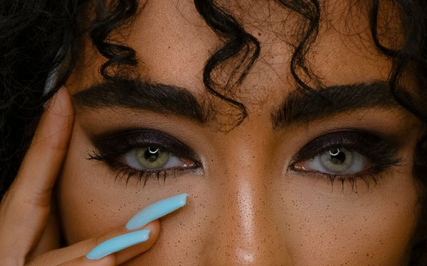 Model with deep skin tone wearing gray-green colored contacts with smoky liner