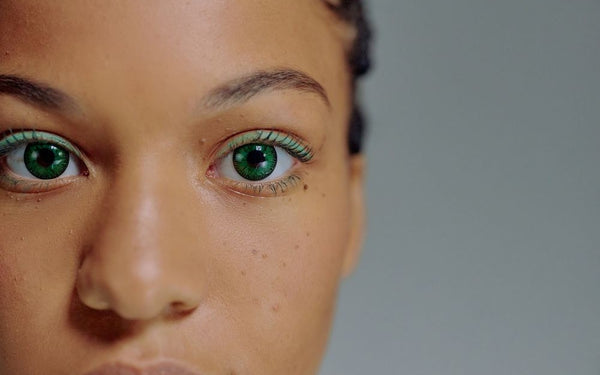 Model with deep skin tone wearing vivid green colored contacts, direct gaze