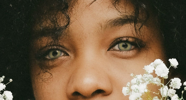 Horizontal close-up of a deep-skinned model wearing light colored contact lenses beside white flowers