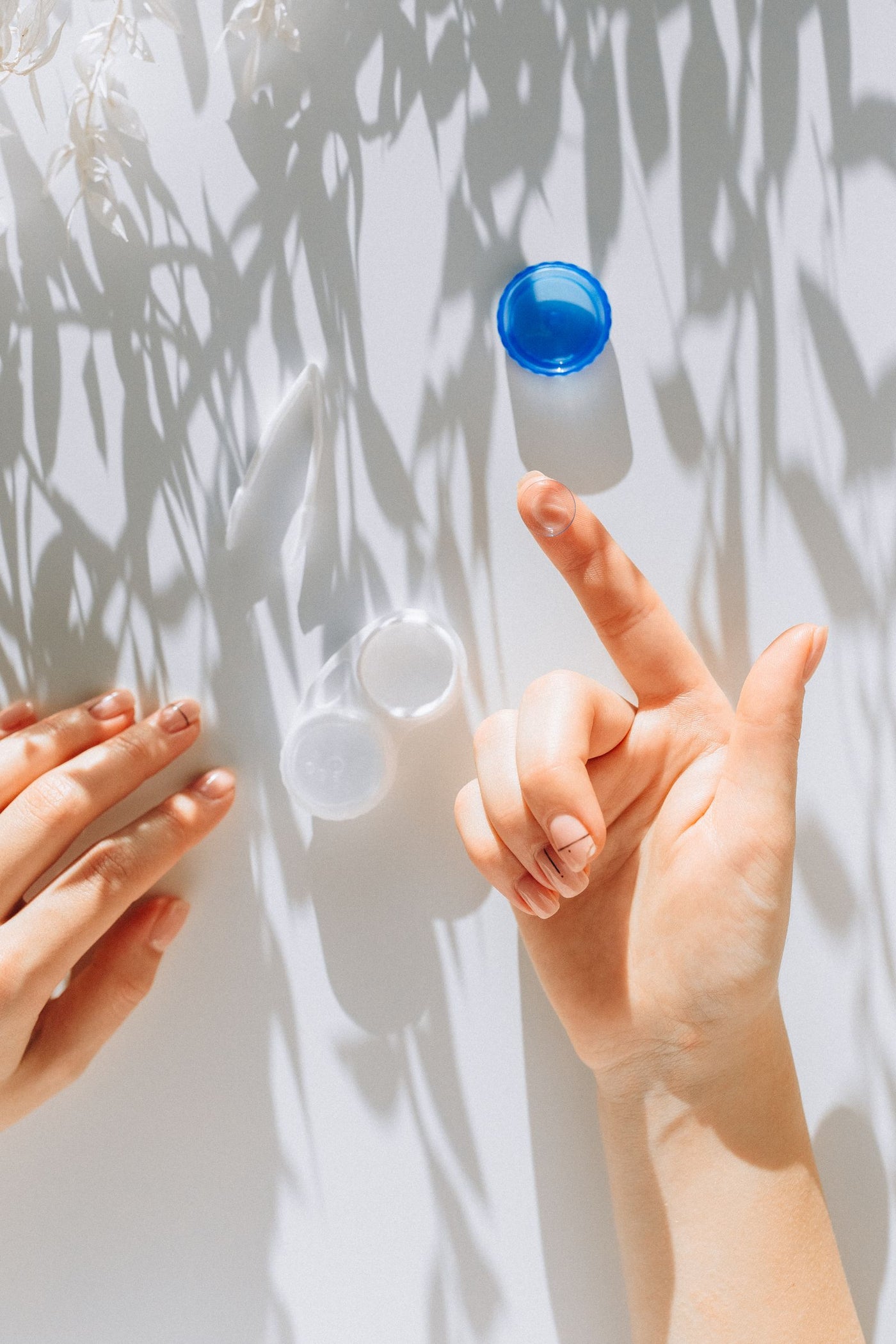 Hands holding a contact lens near its container in soft sunlight