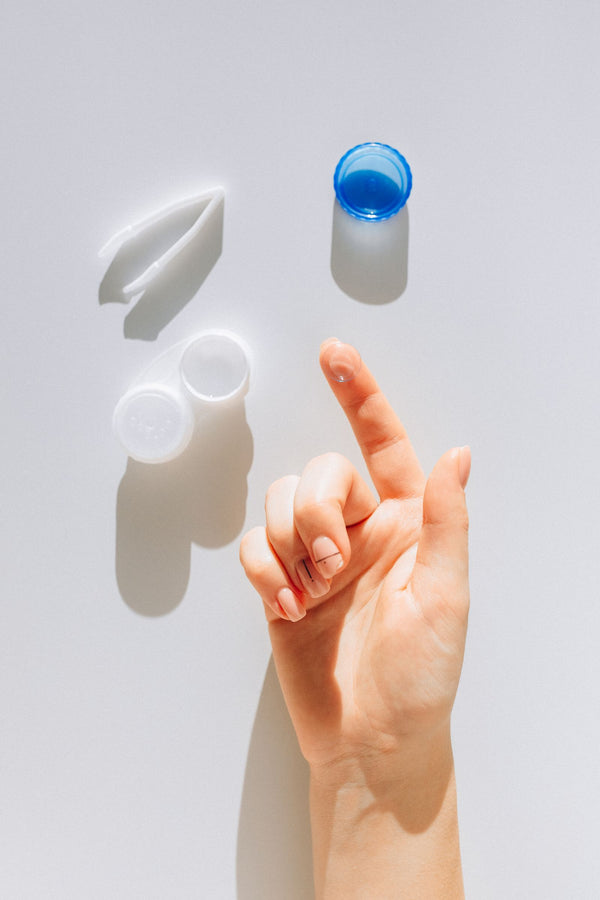 Hand holding a contact lens beside its case and solution