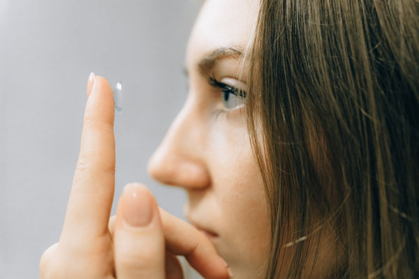 Young woman holding a contact lens on her fingertip in front of her eye