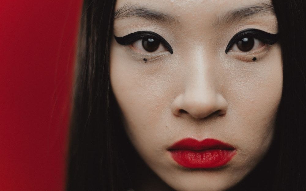 Sharp winged siren eyeliner with red lips on an East Asian model, direct gaze