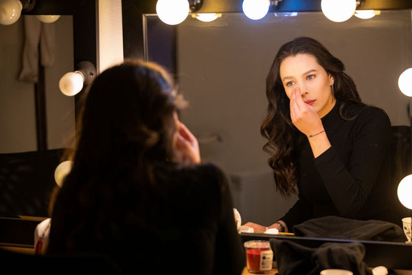Woman perfecting natural makeup at a bright vanity mirror — polished but effortless