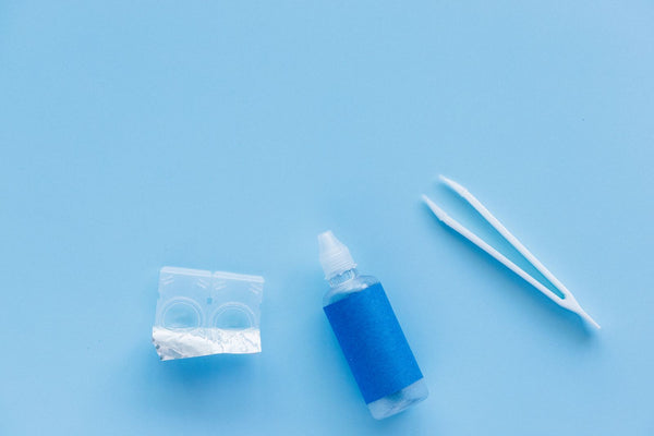 Contact lenses, solution bottle and tweezers arranged on a blue background