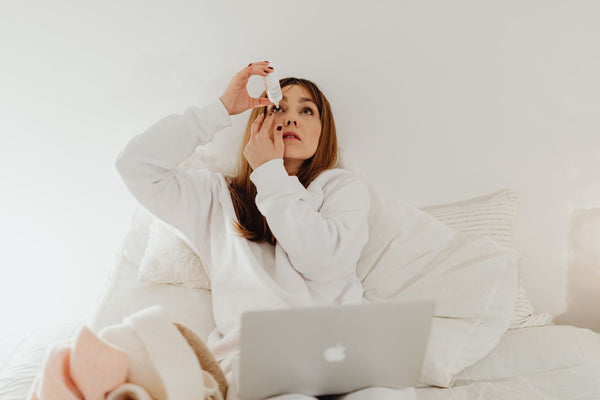 Woman using contact-safe rewetting eye drops while working on a laptop in bed