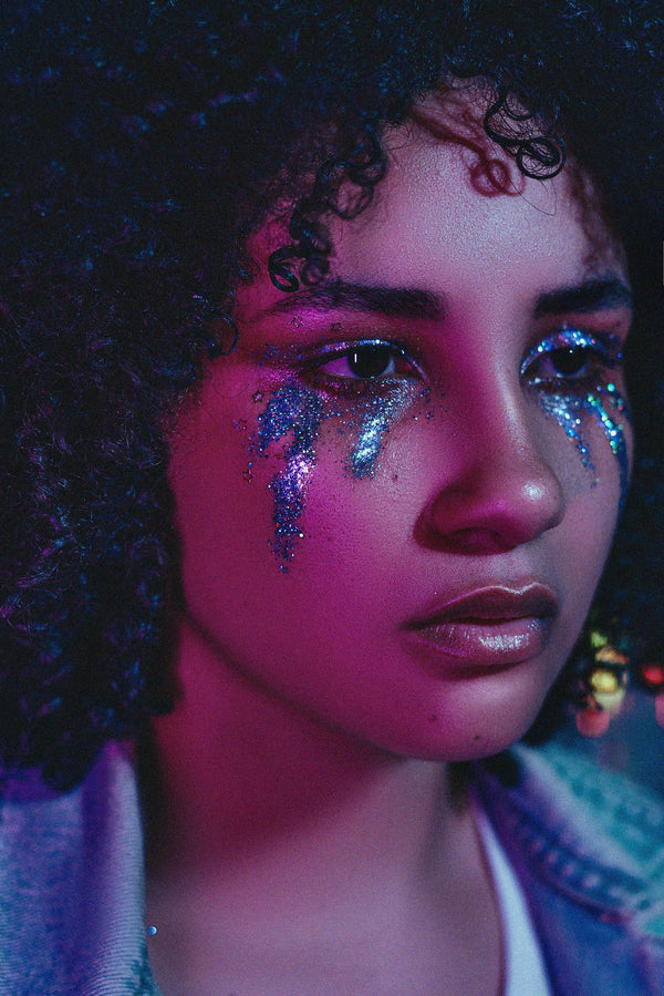Glitter-tear makeup under both eyes in purple neon light — the Euphoria-inspired aesthetic